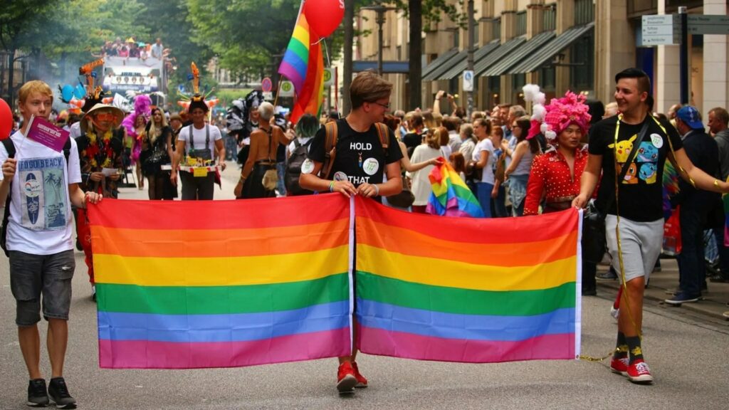 three men in a parade holding a lgbt flag